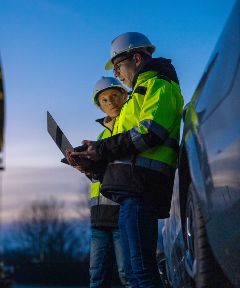 Two petroleum engineering professionals look at a laptop in the field next to an oil pump