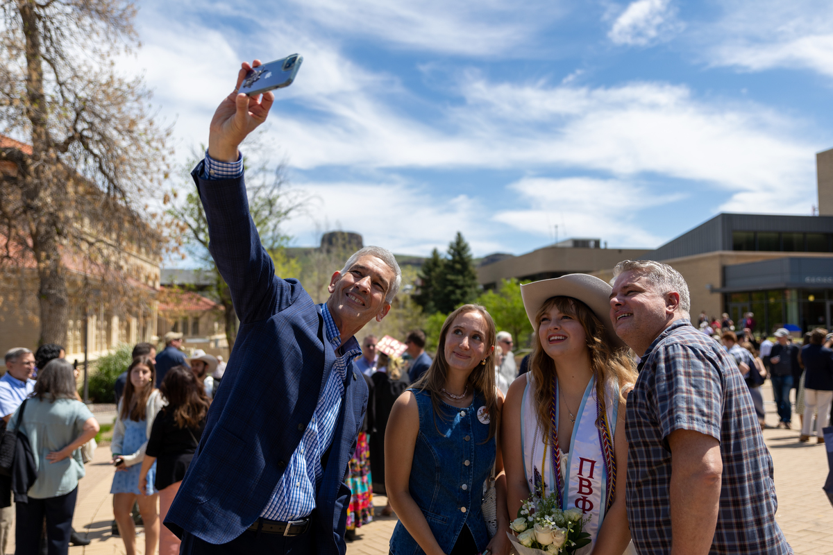 Mines President Paul C Johnson takes a selfie with an undergraduate and her parents at graduation.