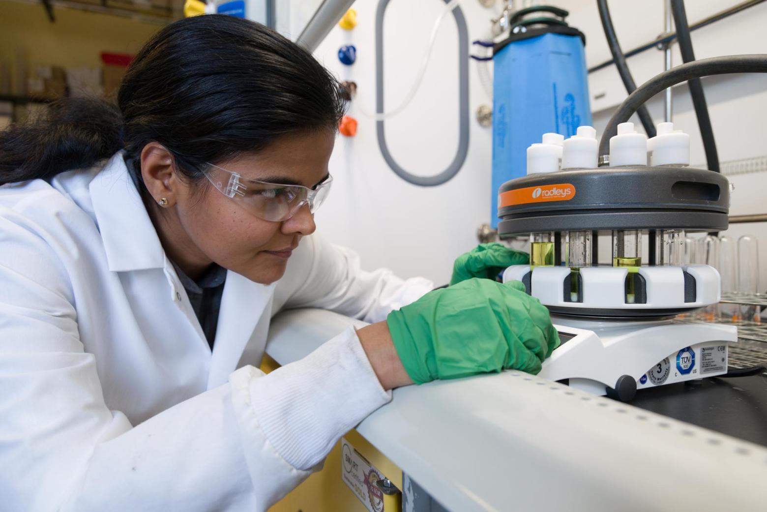 ramya kumar in lab coat and green gloves working in lab