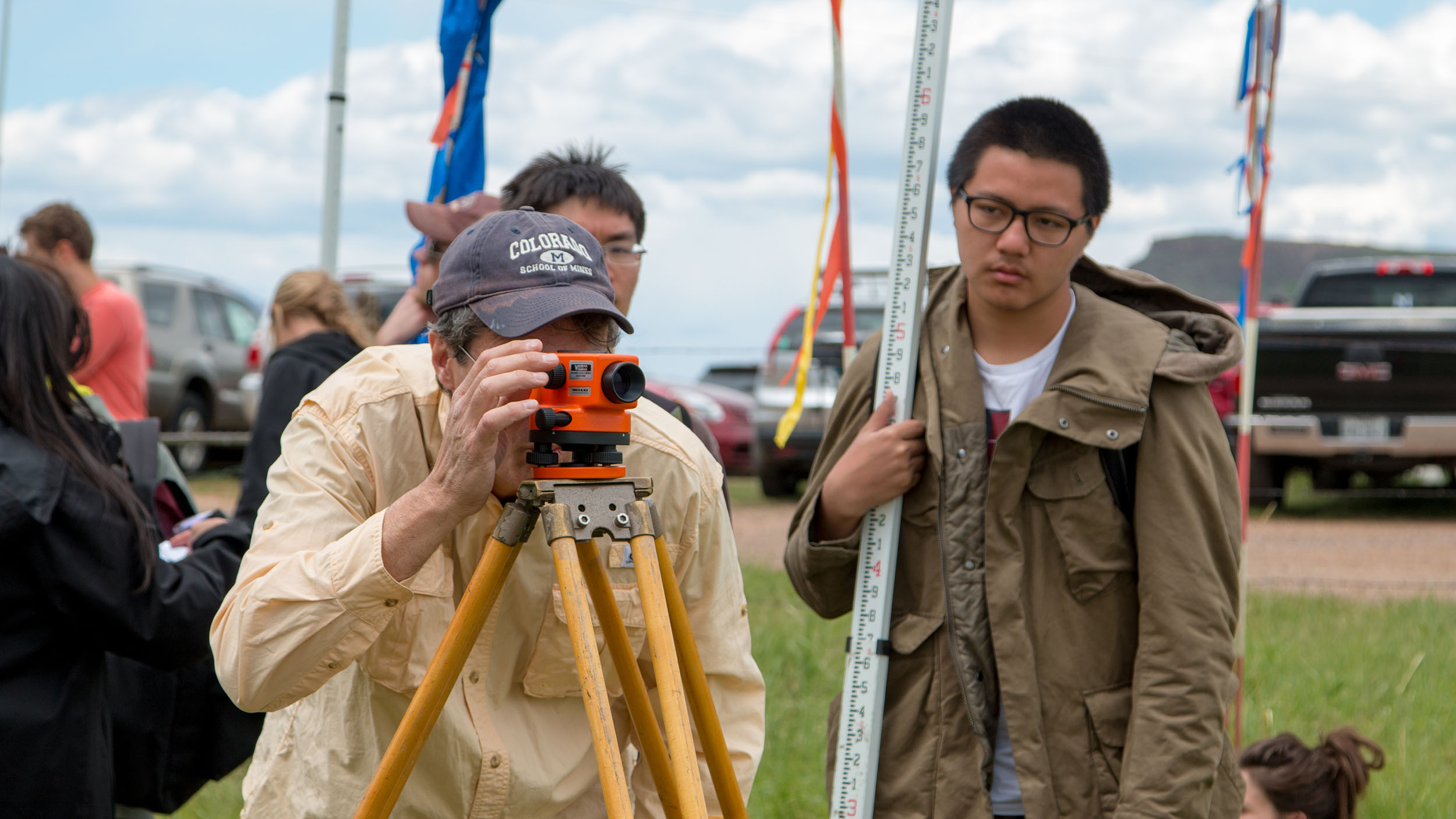 A group of people standing around a man using a theodolite.