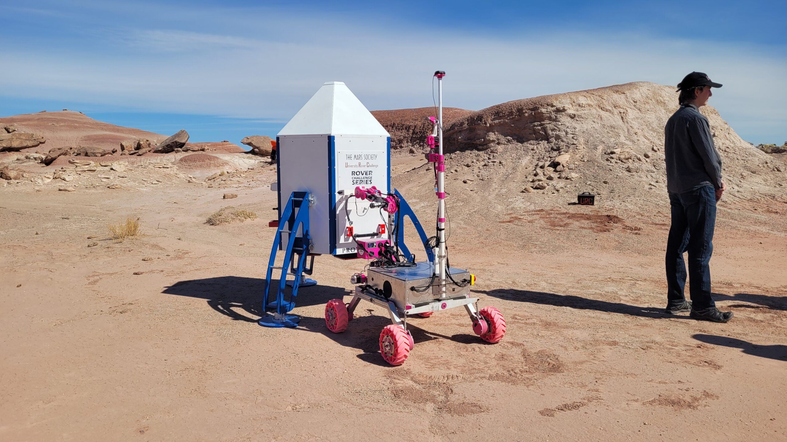 A man standing next to a small robot in the desert.