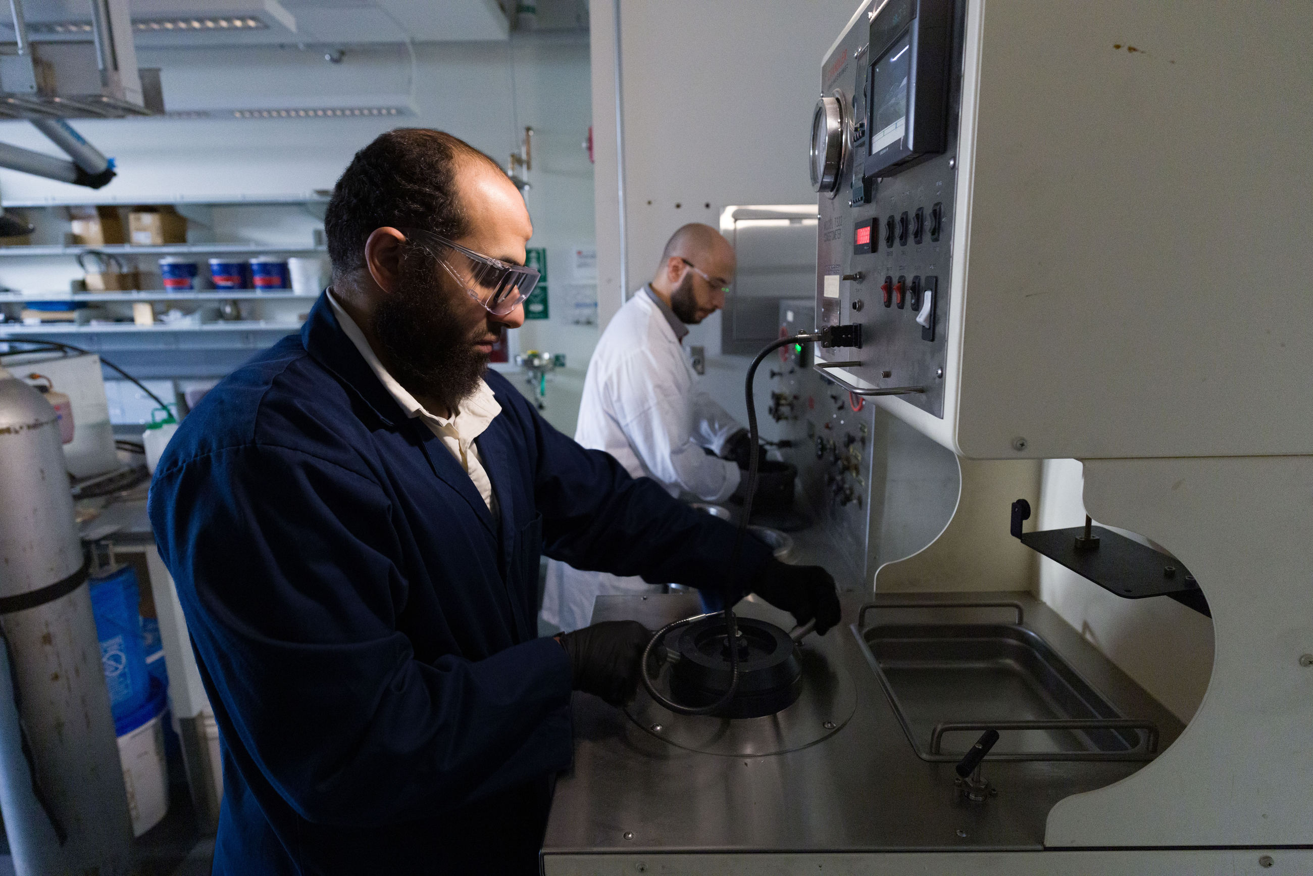A man in a lab coat and goggles working on a machine.